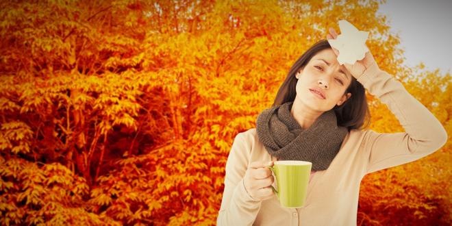 A sick woman holding a mug and a tissue in autumn